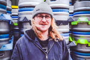 Person standing in front of stacks of metal kegs in a warehouse setting